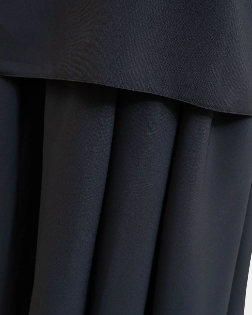 Ourlet du khimar gris foncé retombant sur la jupe assortie, finition surpiquée