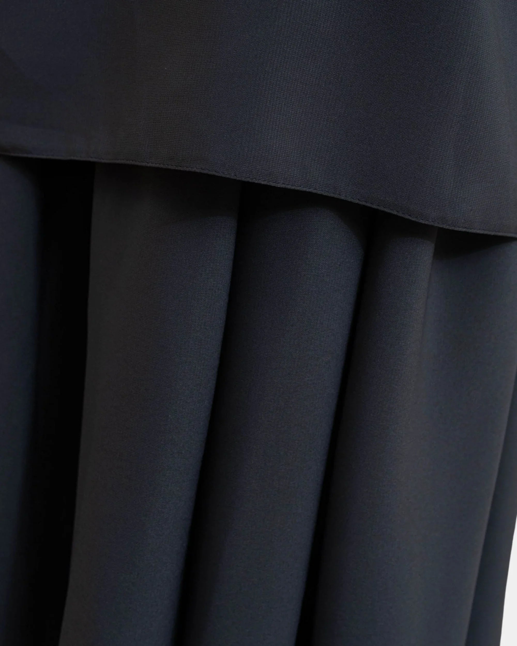 Ourlet du khimar gris foncé retombant sur la jupe assortie, finition surpiquée